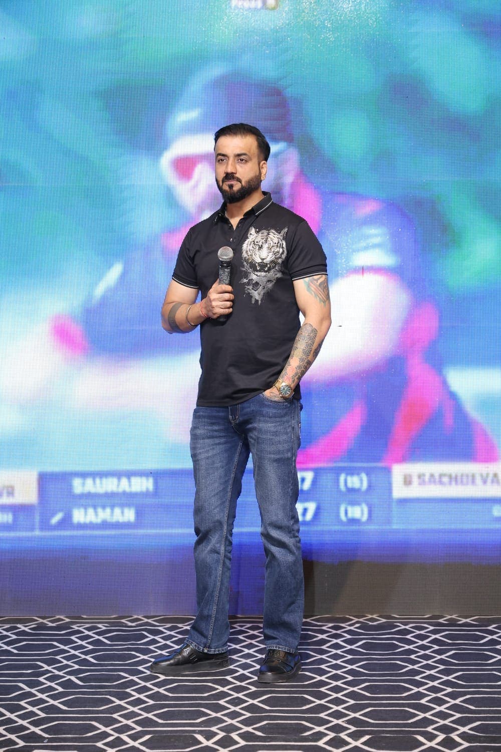 Founder speaking on stage with the live scoreboard behind.